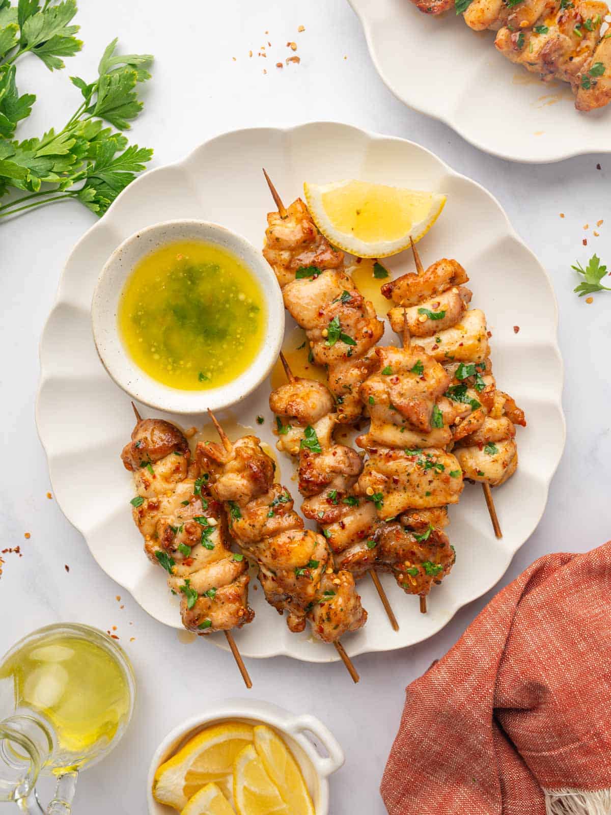 Golden Brown Air Fryer Chicken Skewers on White Plate with Fresh Parsley and Lemon Wedges.