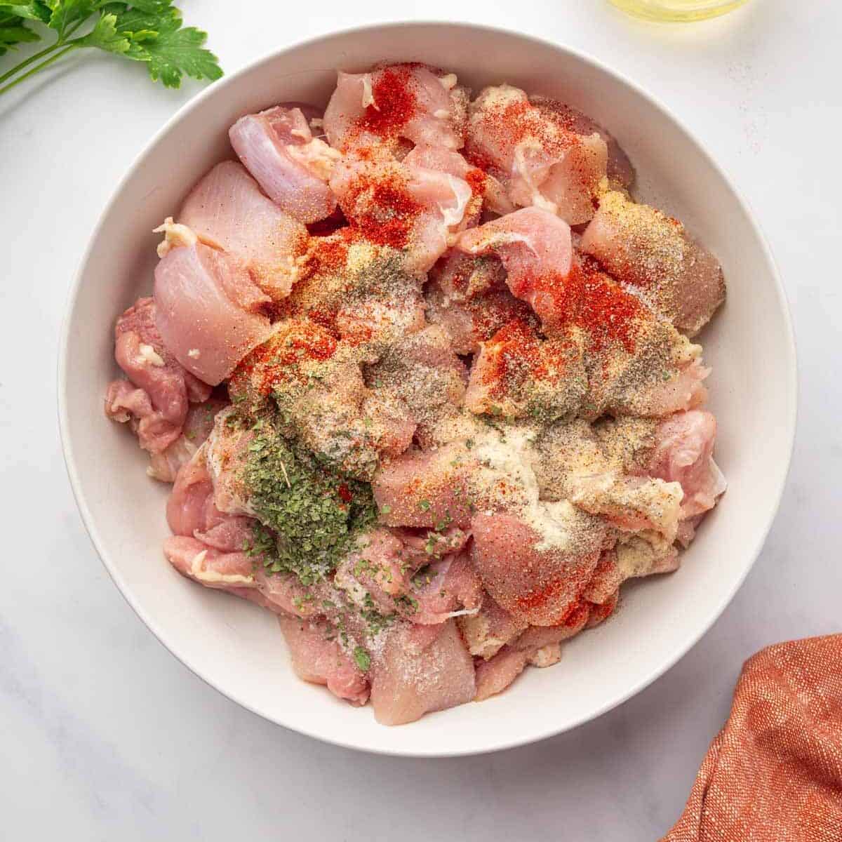 Cubed chicken thighs are seasoned in a bowl.