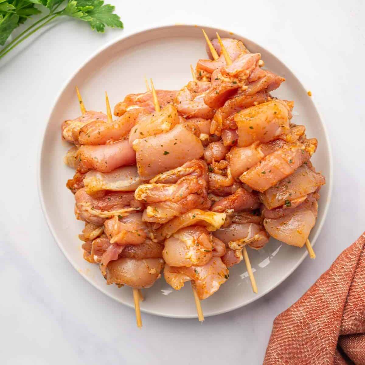 Chicken is threaded onto skewers and marinated, placed on a white plate.