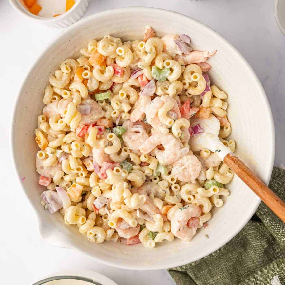 A spatula is used to combine macaroni, shrimp and salad dressing.