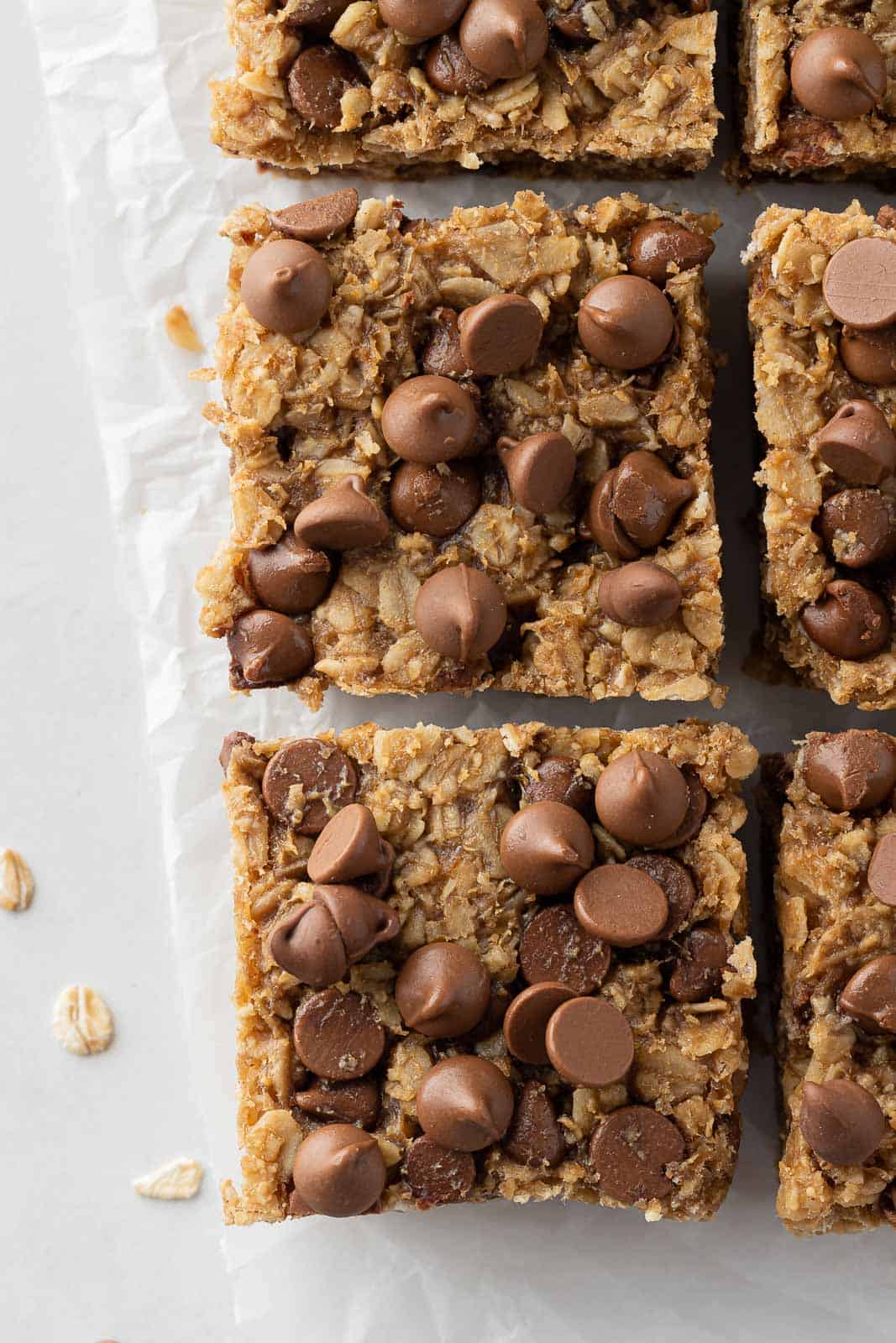 Closeup of two chocolate chip peanut butter oatmeal bars on parchment.