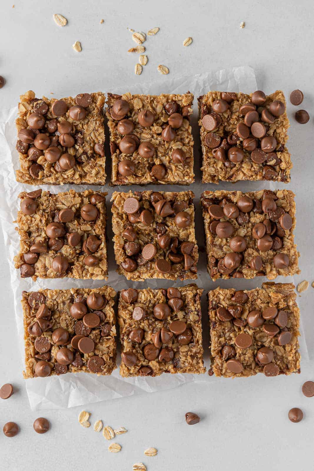 Nine peanut butter oatmeal bars on parchment paper topped with chocolate chips.