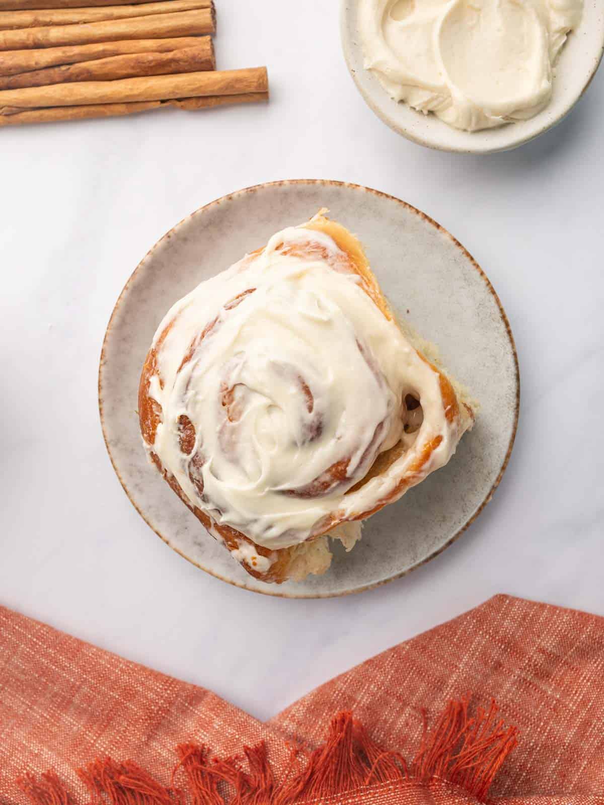 A single cinnamon roll topped with cream cheese icing on a plate.
