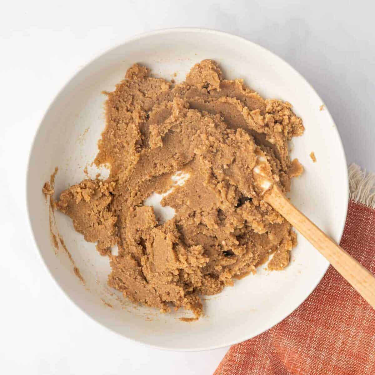 Cinnamon roll filling is mixed in a white bowl with a wooden spoon.