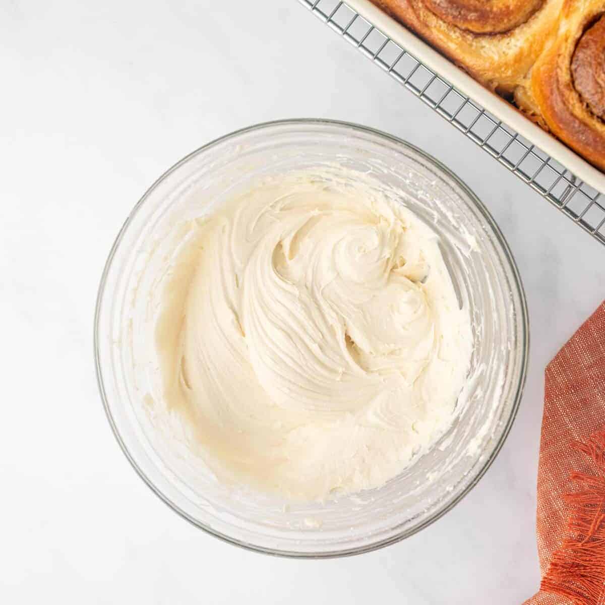 Cream cheese frosting for cinnamon rolls in a clear bowl.