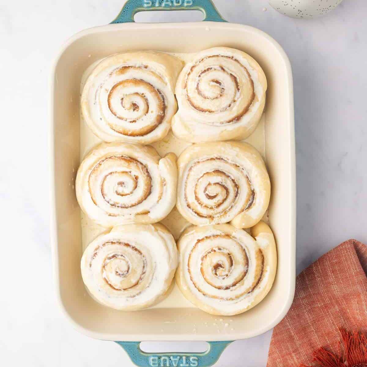 Heavy cream is added to unbaked cinnamon rolls in a rectangle baking dish.