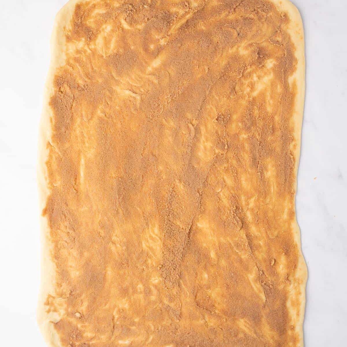Cinnamon sugar mixture is spread onto the rolled out cinnamon roll dough.