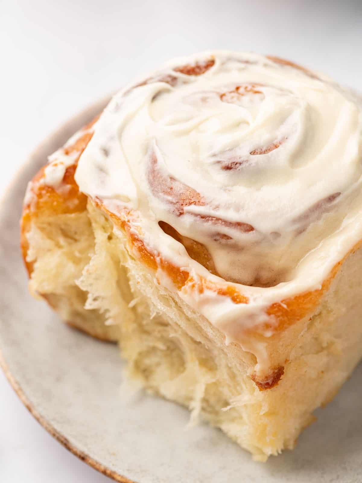 Close up of a flaky cinnamon roll topped with cream cheese frosting on a plate.