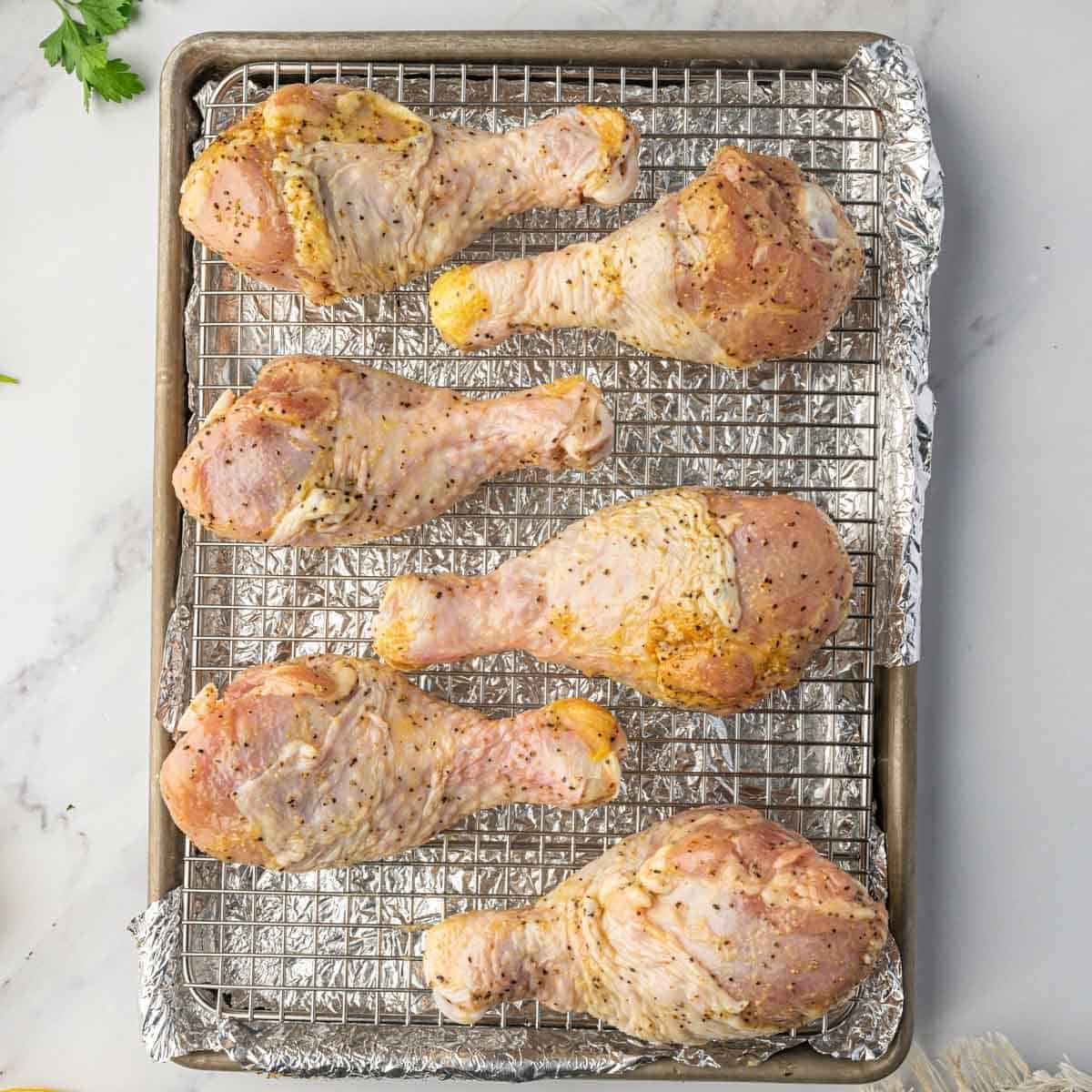 Uncooked chicken legs on a baking sheet with a wire rack.
