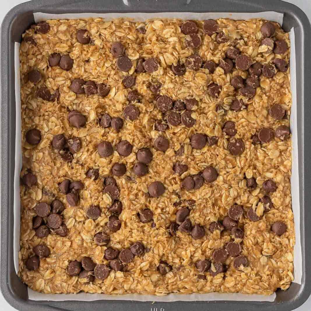 Uncooked oatmeal bar batter pressed into a square baking pan lined with parchment.