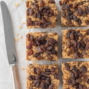 A knife rests beside six cut cinnamon raisin oatmeal bars.