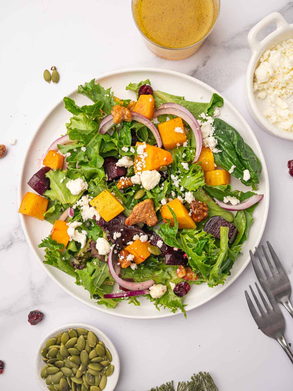 A single serving of salad with butternut squash and feta is on a round white plate.