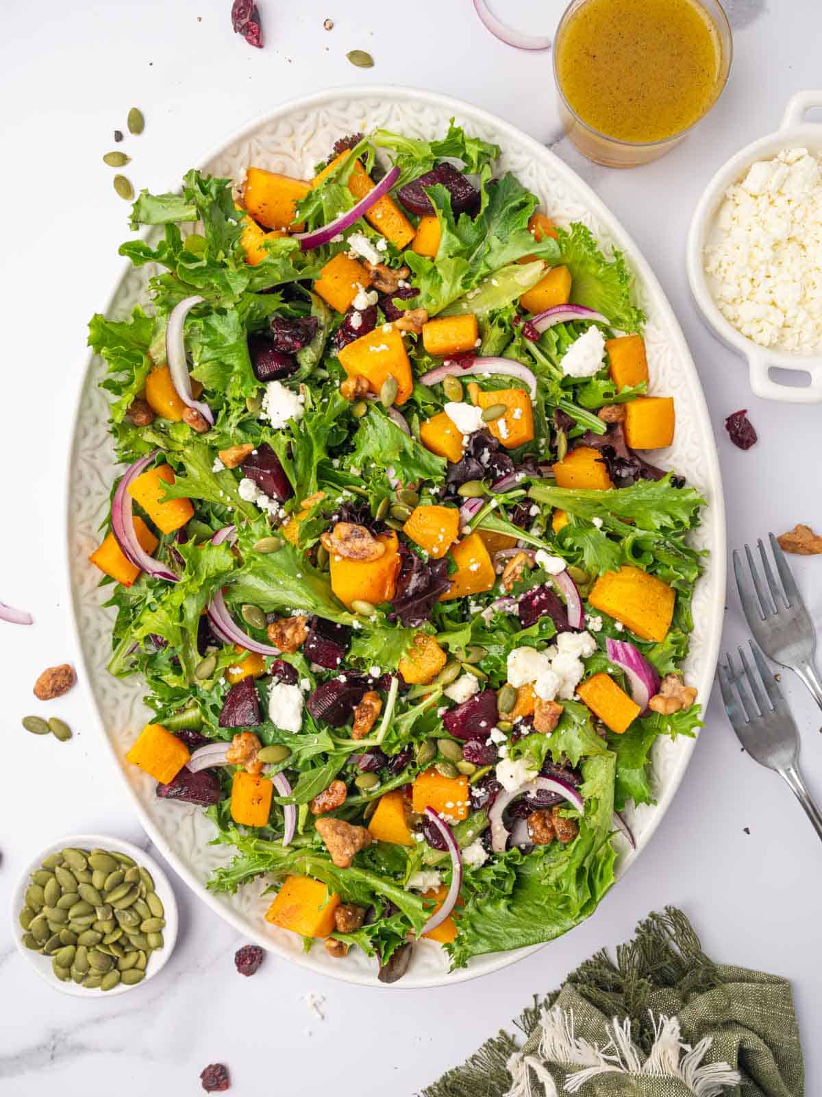 A large platter with a green salad topped with butternut squash, red onion and feta cheese.