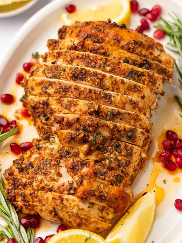 Sliced, roasted turkey breast with cajun spices on a platter gernished with pomegranate and rosemary.