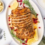 Sliced cajun turkey breast on a large platter with garnishes of rosemary, lemon and pomegranate seeds.