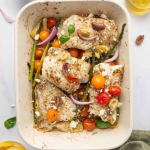 Seasoned cod fish in a rectangle baking dish with asparagus, tomatoes and onions.