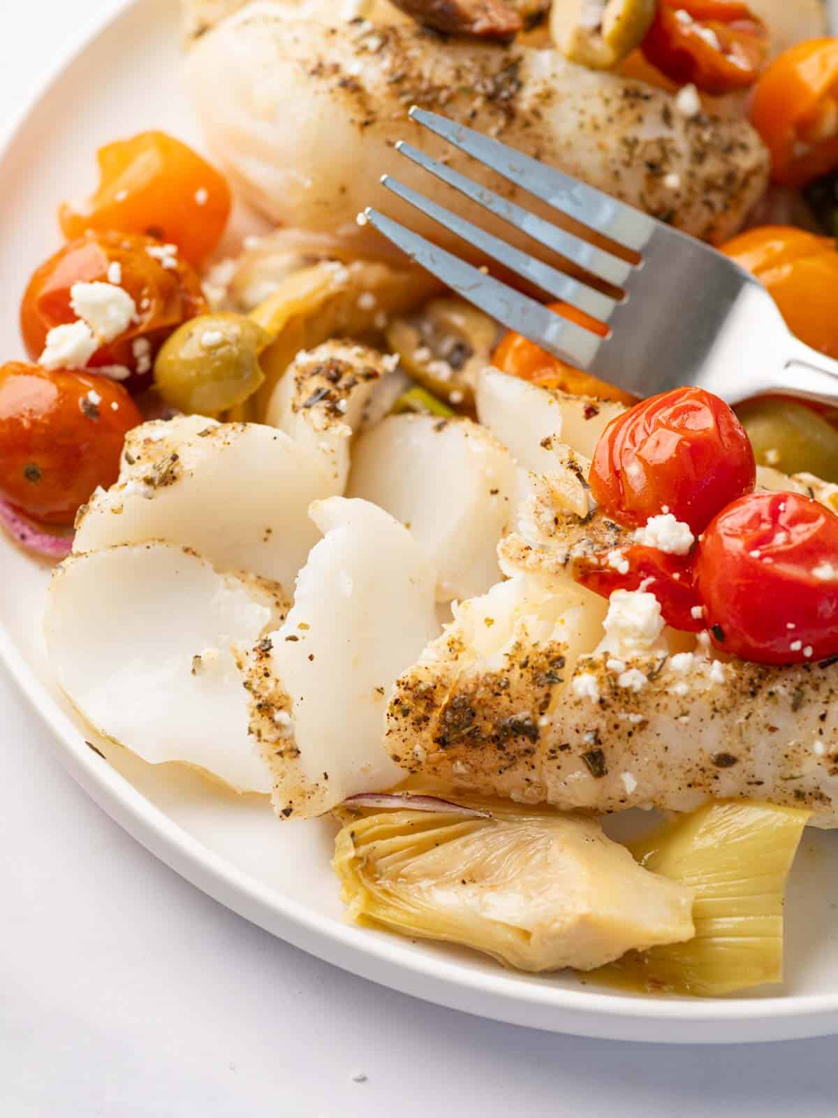 A fork flakes a piece of mediterranean cod.
