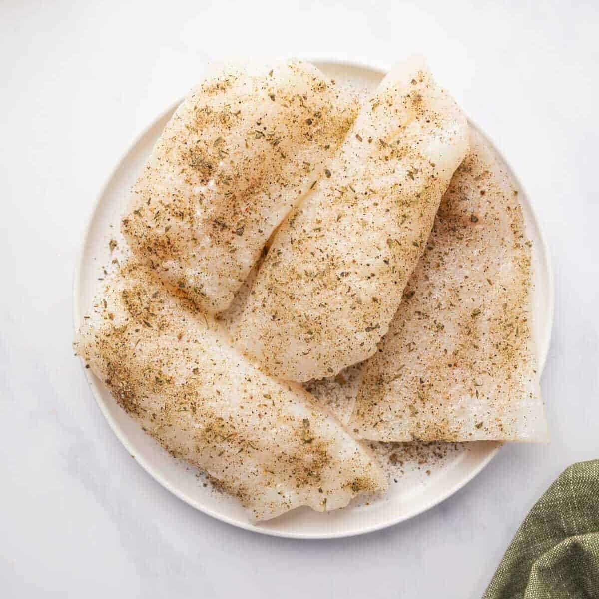 Seasoned cod filets are on a plate.