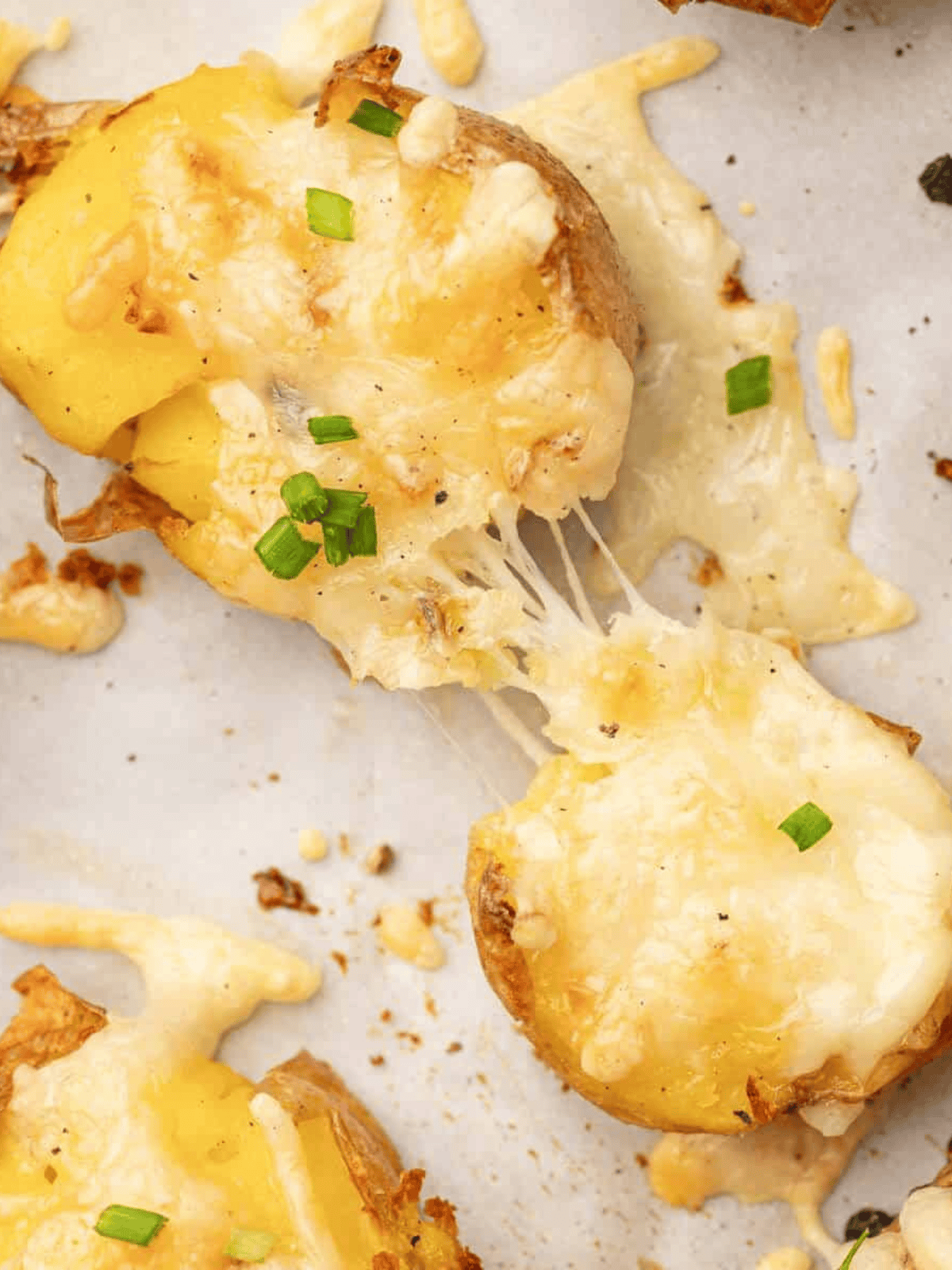 Golden baked smashed potatoes topped with melted mozzarella and fresh chives on a baking tray.