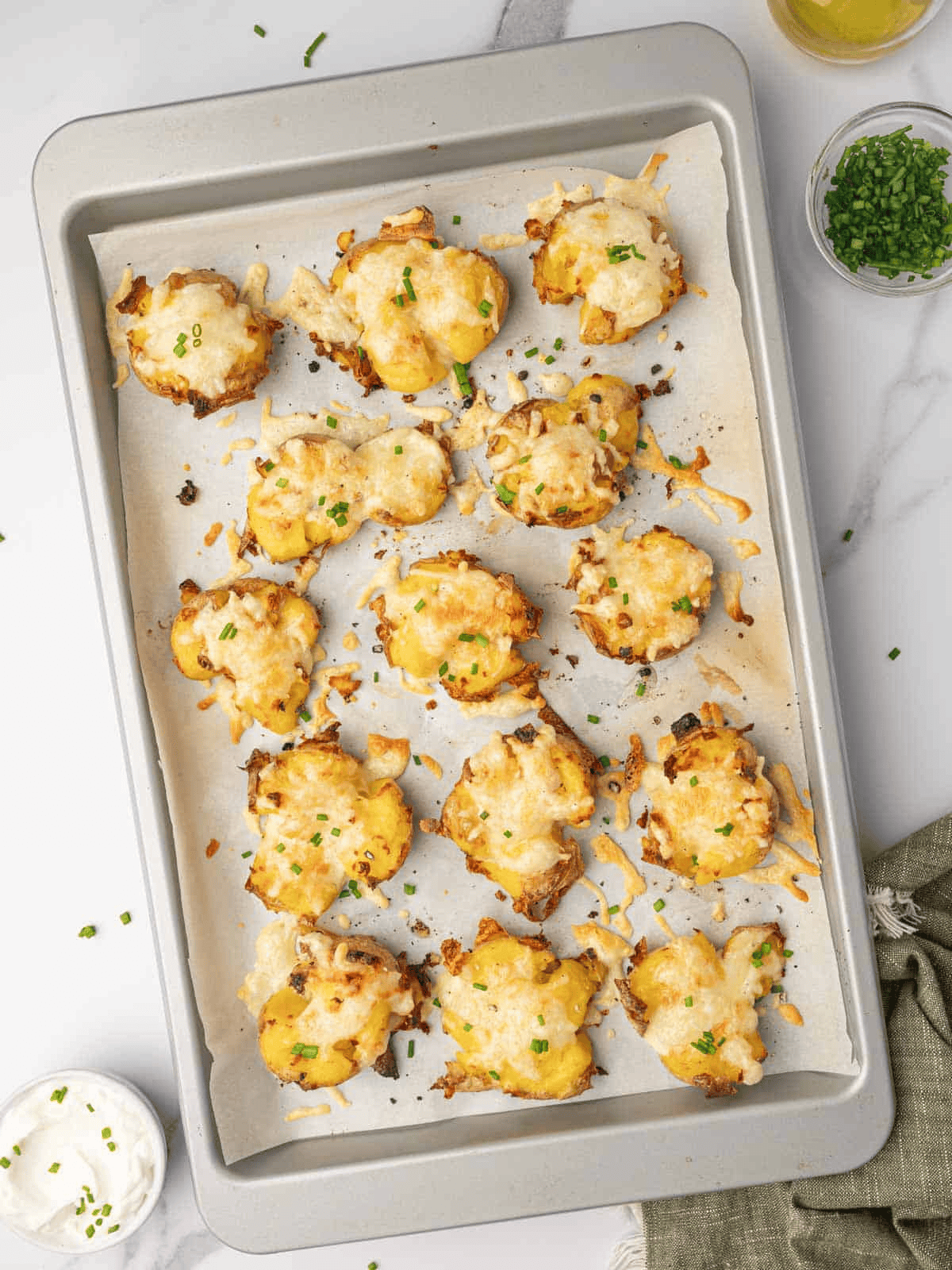 Cheesy Smashed Potatoes with golden melted cheese and chopped fresh chives on a baking tray.
