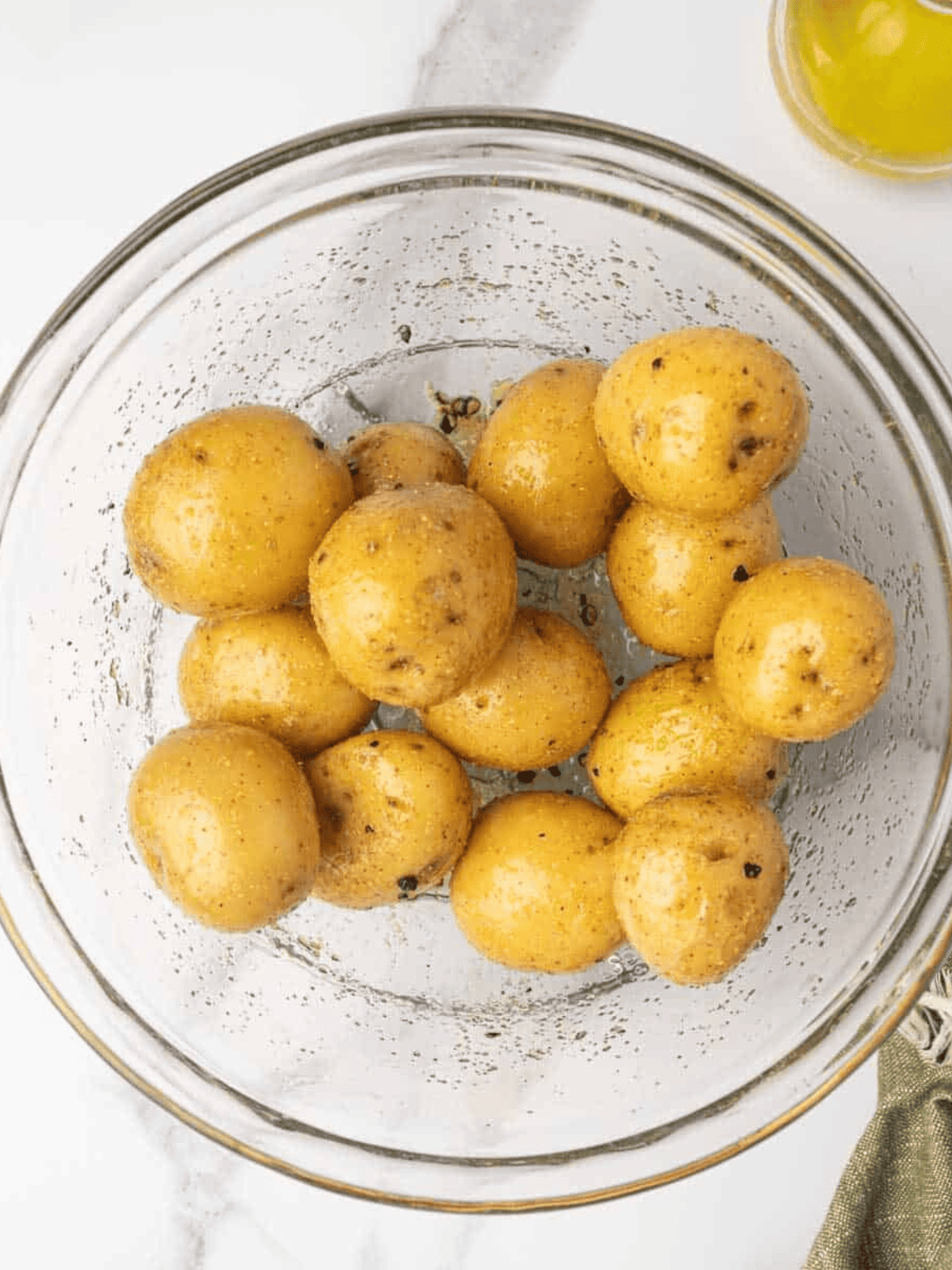 Tender Yukon gold potatoes tossed with olive oil, garlic powder, salt, and cracked pepper in a glass bowl.
