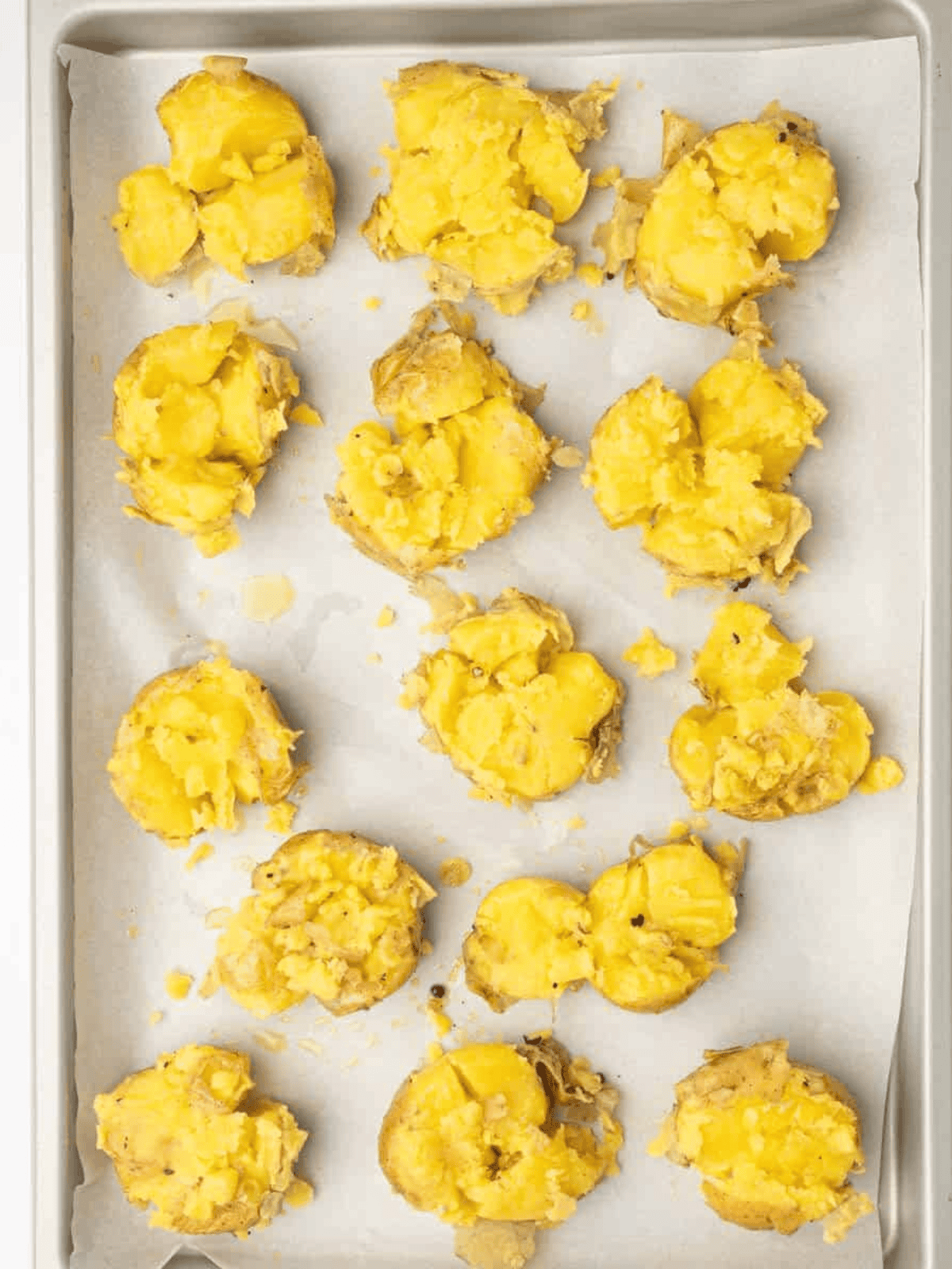 Seasoned smashed potatoes arranged on a parchment-lined baking tray before adding shredded mozzarella.