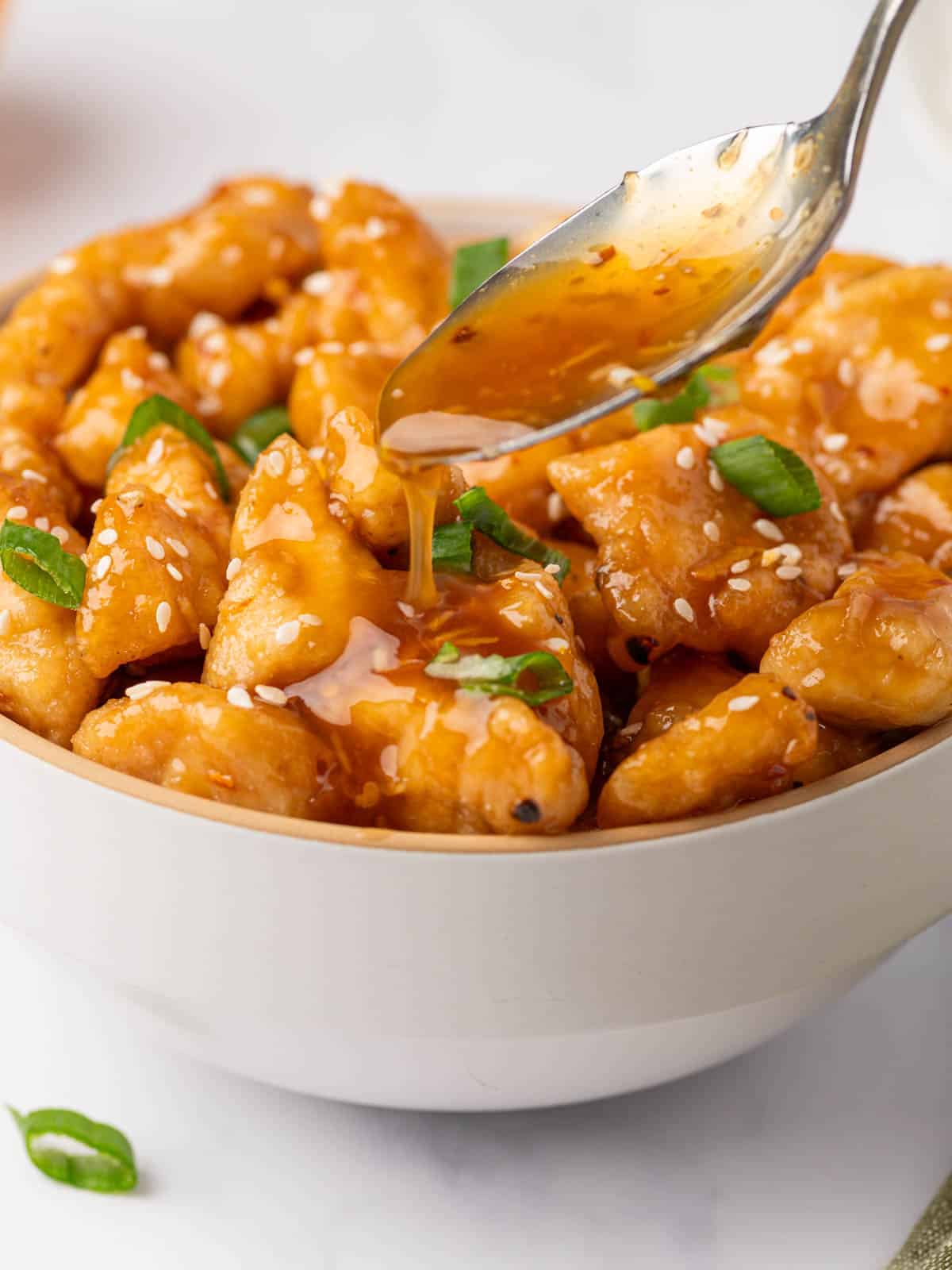 Orange sauce spooned over chicken with green onions and sesame seeds.