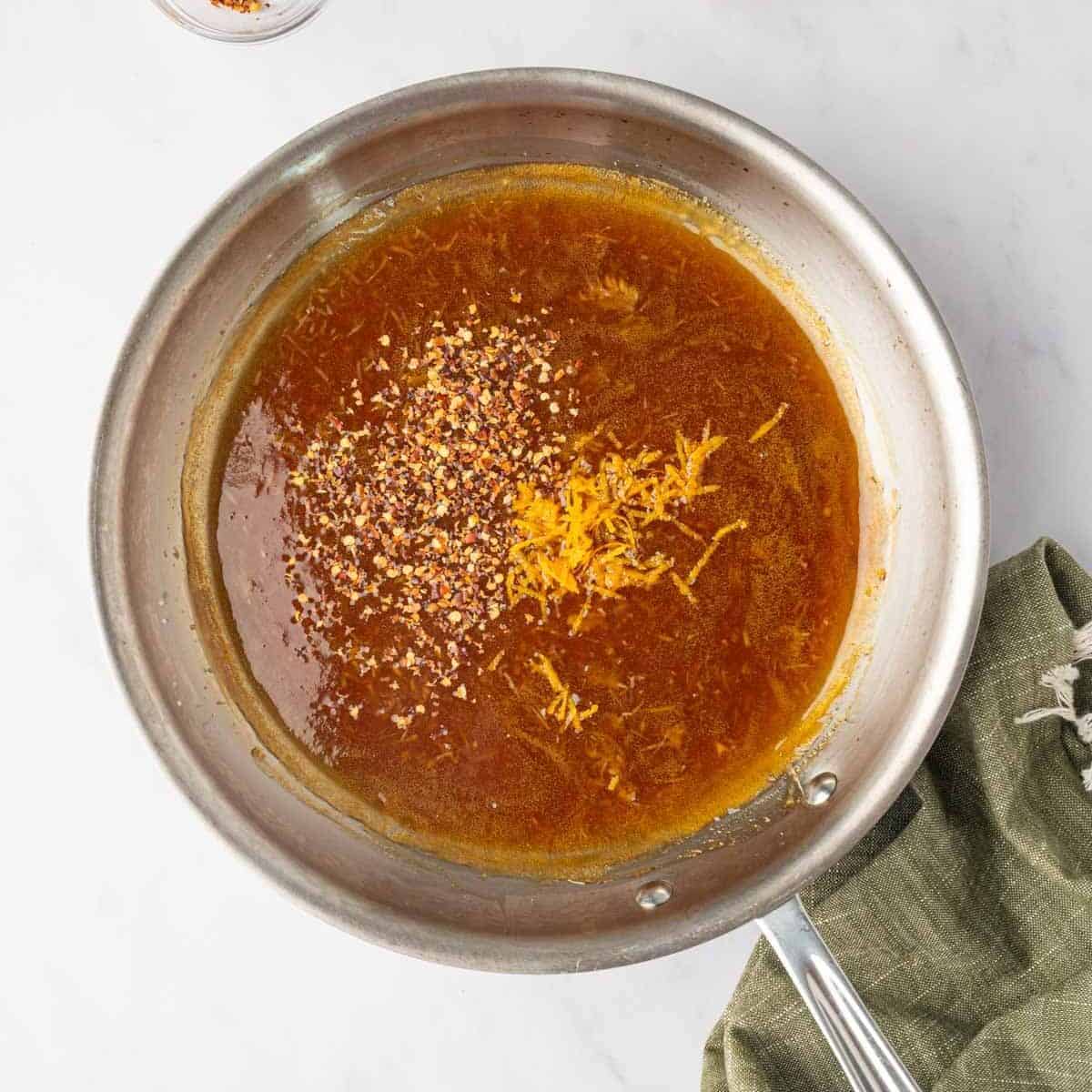 Orange zest and red pepper flakes added to the thickened sauce in a saucepan.