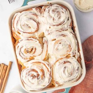 Cinnamon rolls covered with thick cream cheese icing in a white baking dish.
