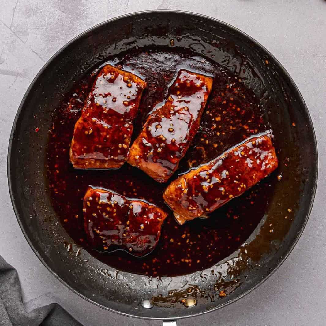 A dark, glossy honey garlic sauce over the seared salmon fillets in the pan.