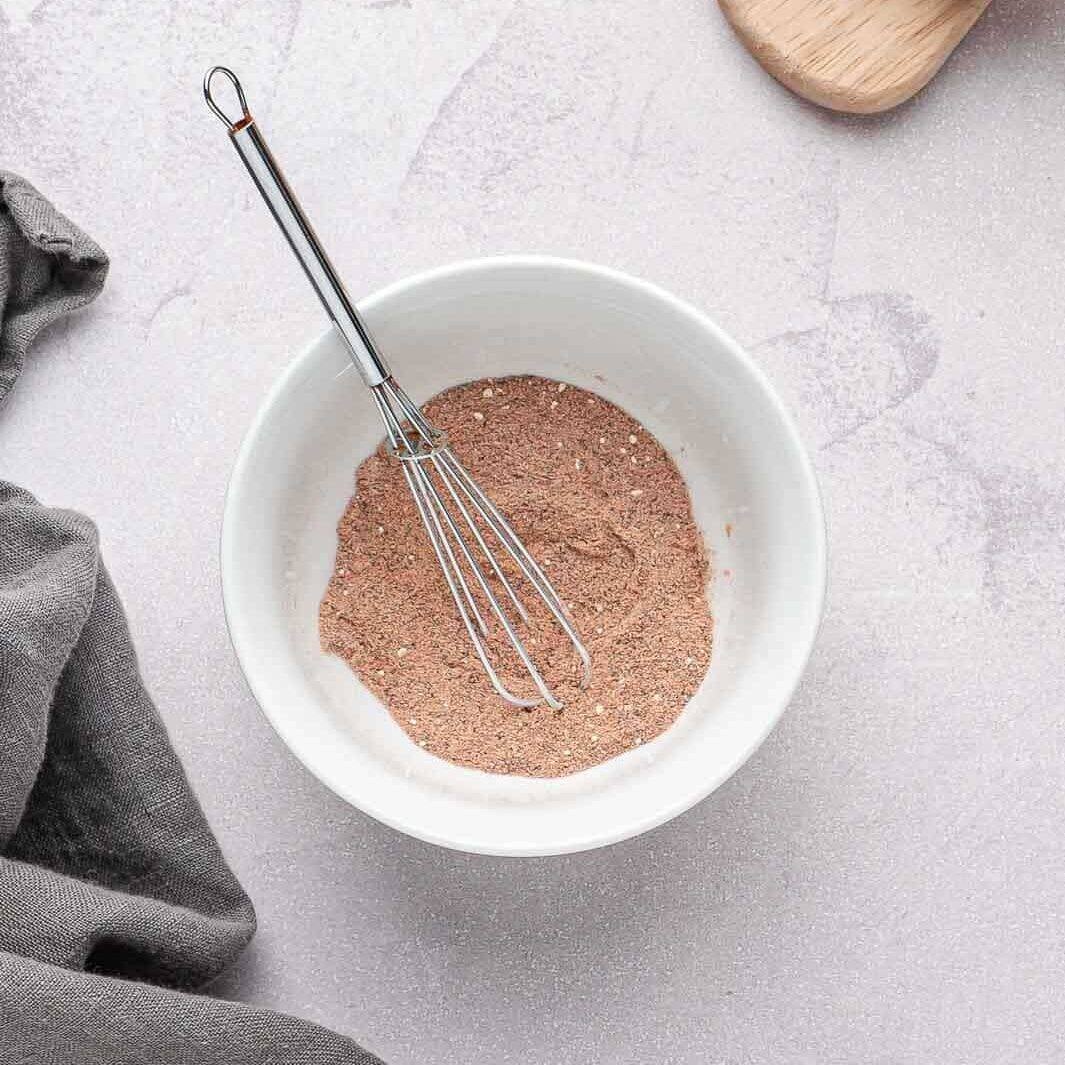 A close-up of a small glass bowl whisking together the smoky dry rub seasoning.
