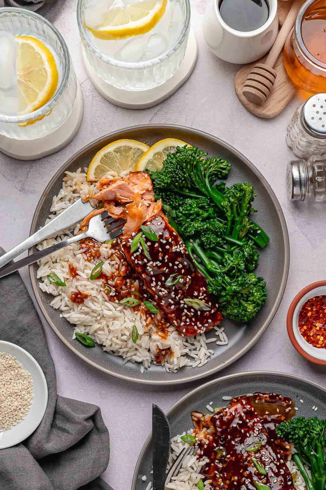 close-up shot of a single, flaky fillet of Spicy Honey Garlic Salmon served over a generous scoop of jasmine rice and nestled next to roasted broccoli florets. The entire plate is drizzled with that signature caramelized glaze and looks like a perfect, balanced weeknight meal.