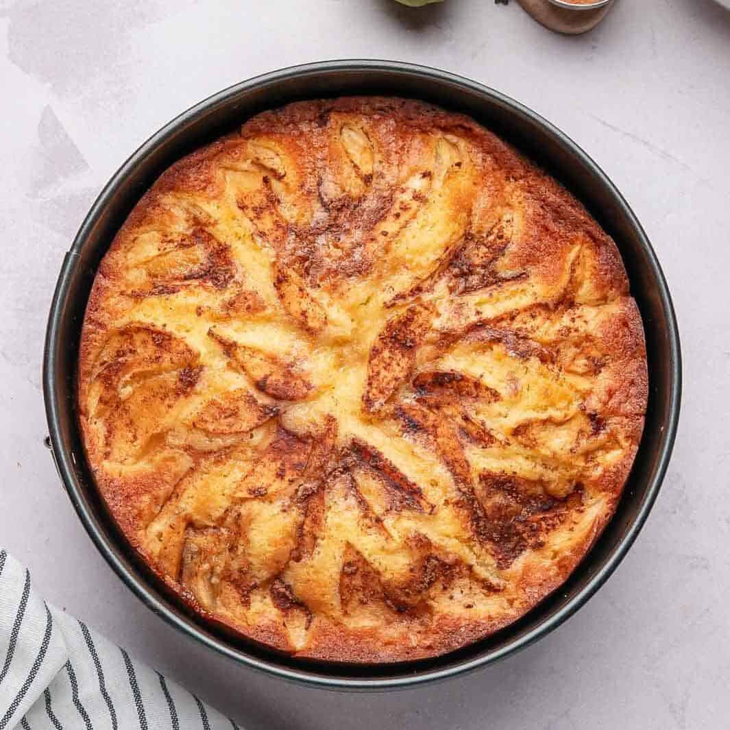 A freshly baked easy moist pear cake with a golden caramelized cinnamon-sugar crust resting in the cake pan.