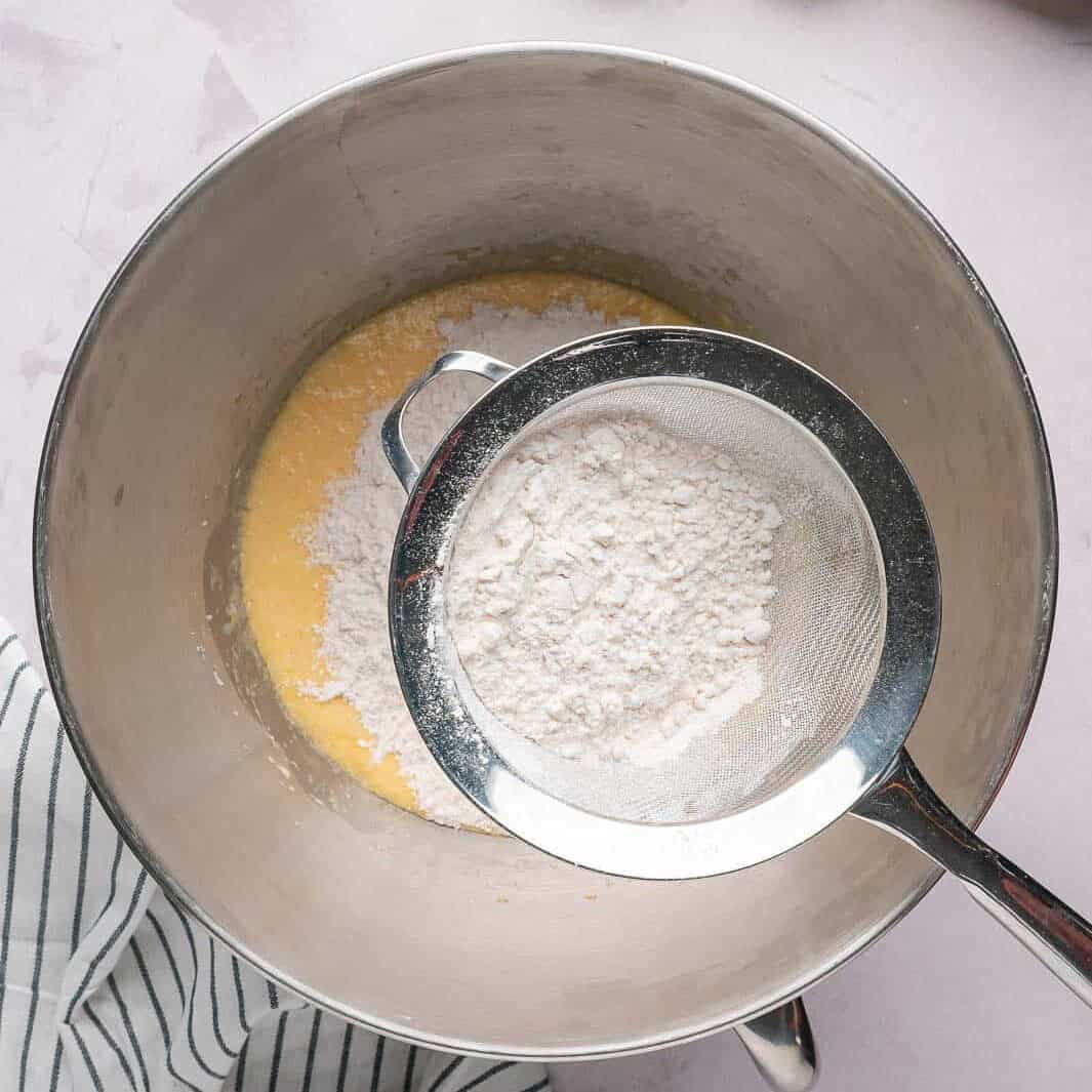 Sifting all-purpose flour and baking powder into the wet ingredients to ensure a tender pear cake crumb without overmixing.