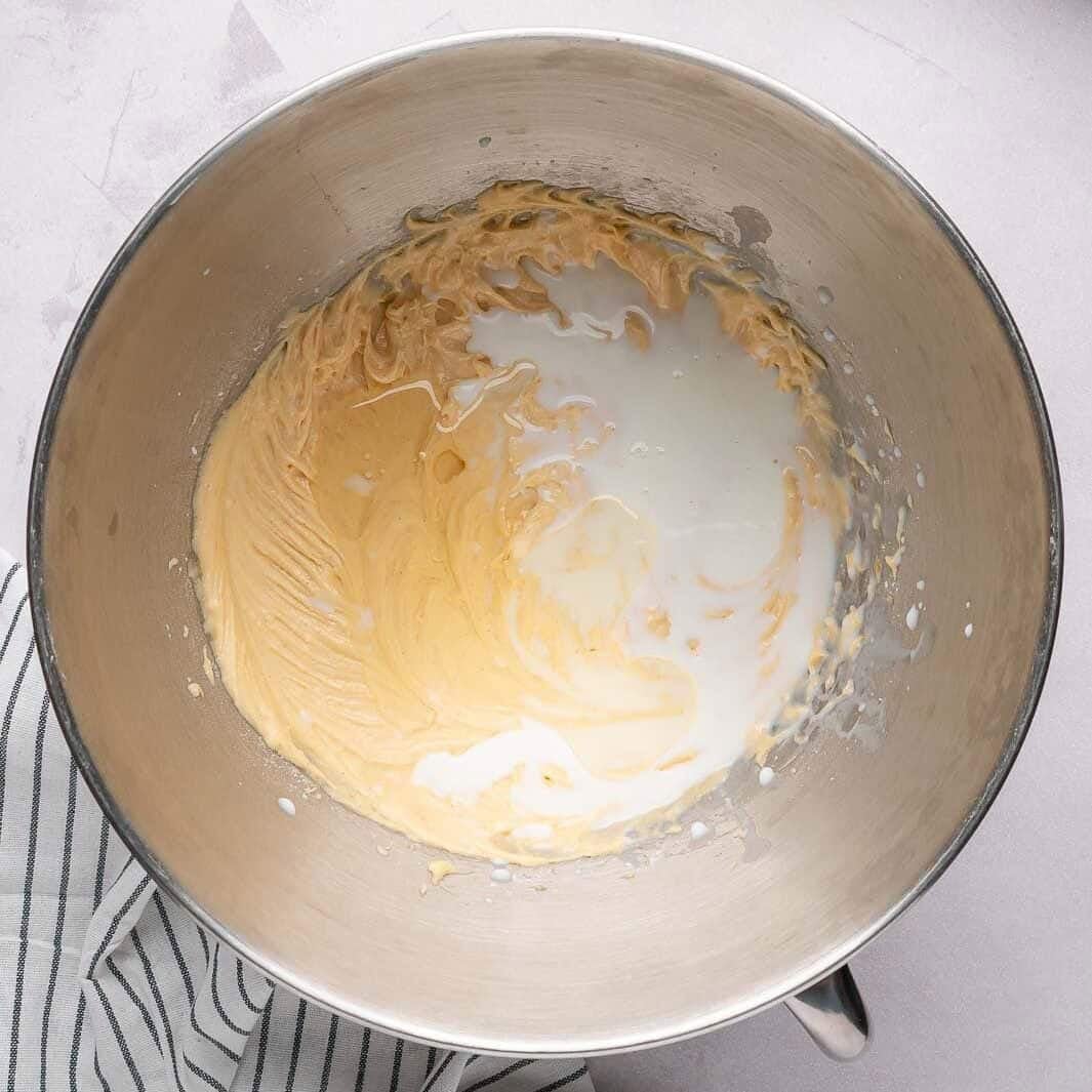 Pouring whole milk into a thick, buttery cake batter and gently folding the mixture together for a smooth, creamy texture.