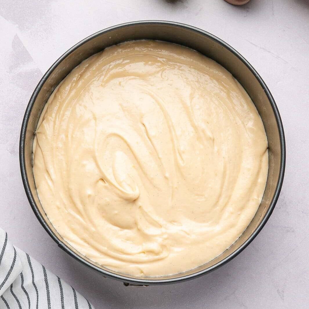 Pouring the smooth, vanilla-flecked cake batter into a pre-greased springform pan to ensure a perfect, non-stick bake for a classic pear cake.