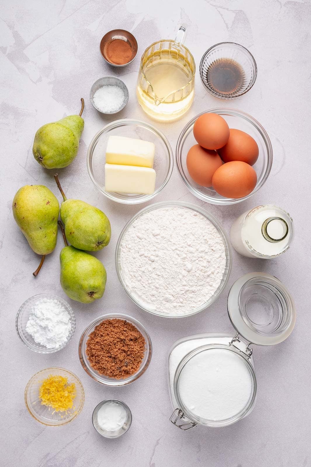 A flat-lay arrangement of fresh Bartlett pears, softened butter, eggs, granulated sugar, and all-purpose flour on a clean kitchen surface, ready for a simple one-bowl pear cake.