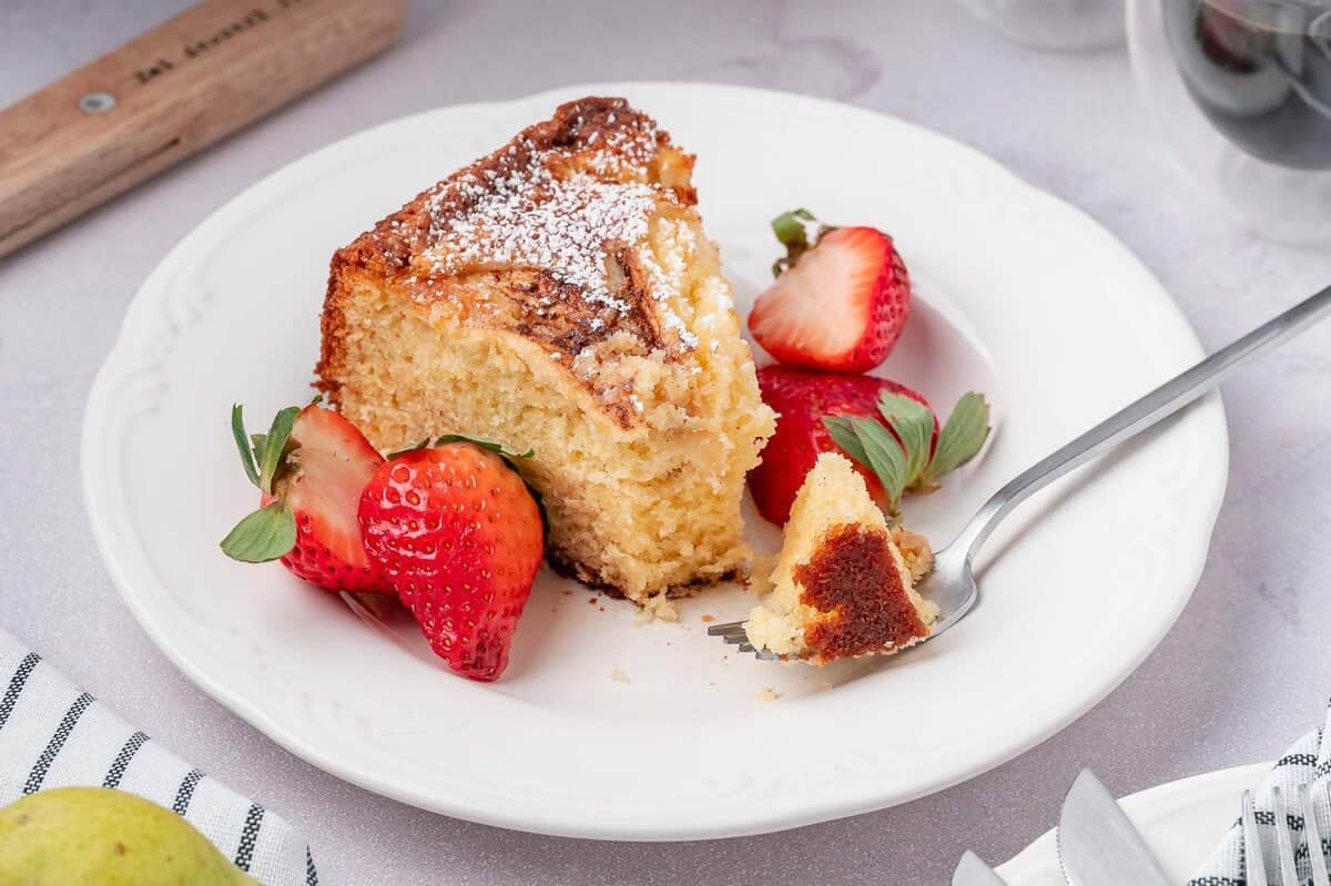 A single slice of easy pear cake on a white plate with a bite taken out, revealing the soft internal texture of the cake.