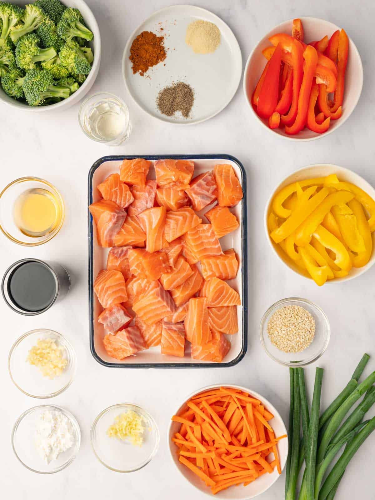 Ingredients for homemade teriyaki salmon stir fry including fresh salmon fillets, broccoli florets, sliced bell peppers, carrots, ginger, garlic, and small bowls of soy sauce and honey.