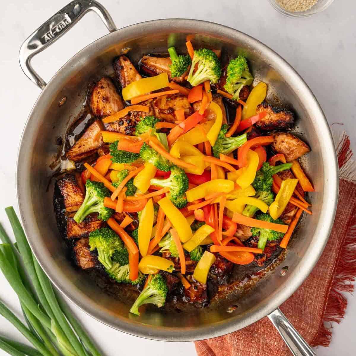 Glossy teriyaki glaze coating salmon and vegetables in a pan.