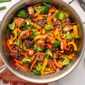 Overhead view of Cookin&rsquo; with Mima's Teriyaki Salmon Stir Fry in a large wok, featuring crispy salmon cubes, bright broccoli, and red bell peppers, served over a bed of fluffy jasmine rice.