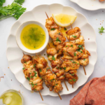 Cooked chicken skewers served with garlic butter sauce, lemon, and fresh parsley.