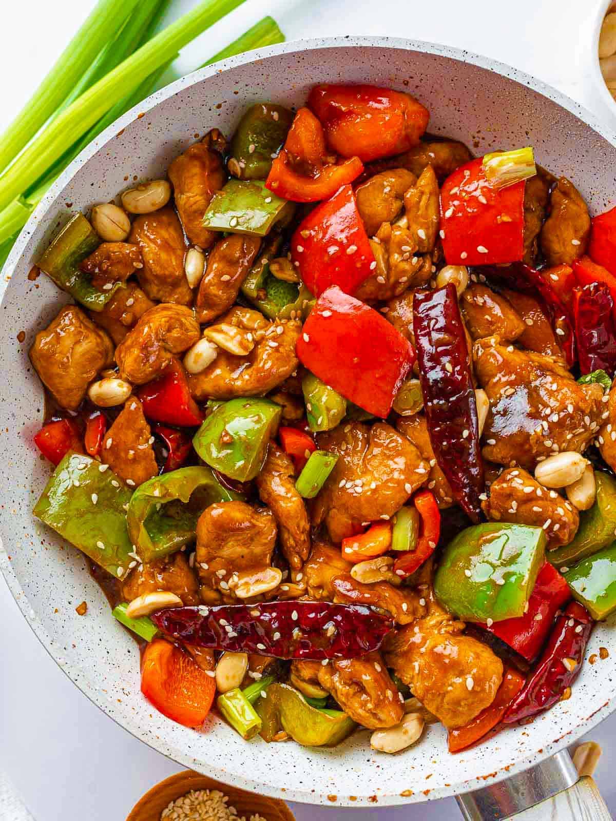 Chicken and bell peppers with peanuts, green onions, and sesame seeds added to the skillet.