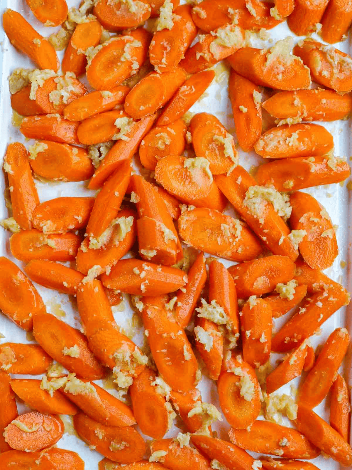 carrots sheet pan Sliced carrots coated with melted butter on a white baking sheet.