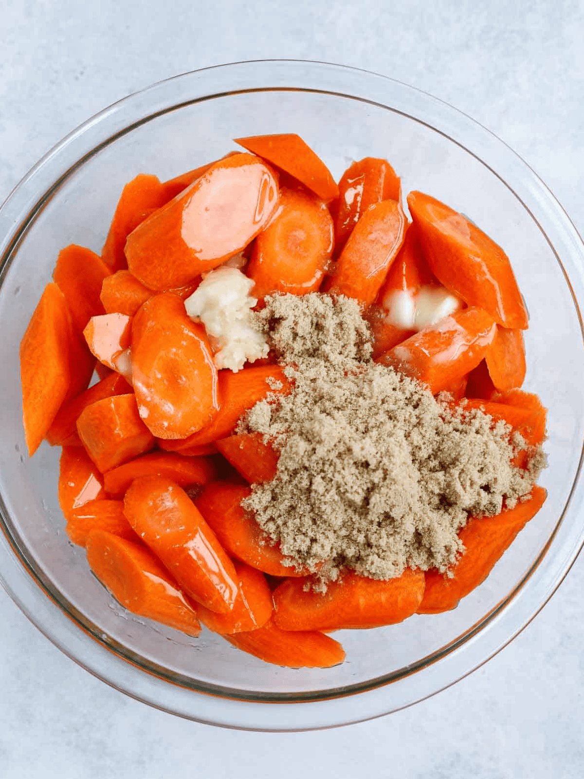 brown sugar carrots Sliced carrots with brown sugar, melted butter, and oil in a glass bowl.