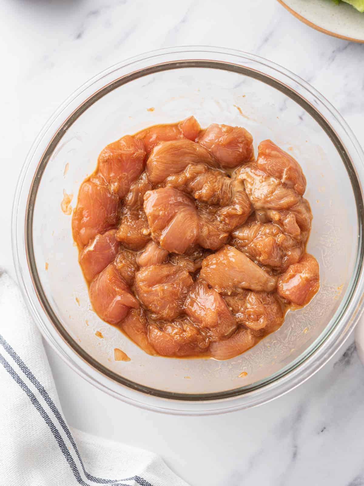 Pieces of chicken coated in marinade in a glass bowl.