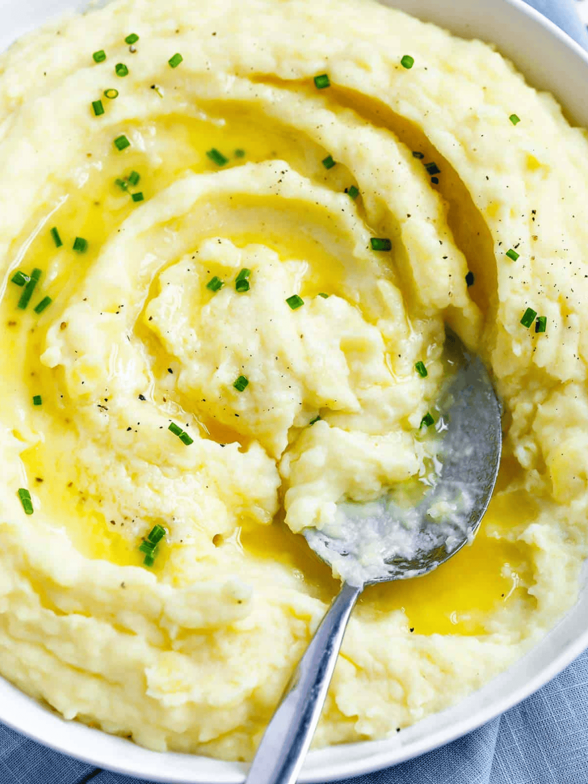 Creamy mashed potatoes in a white bowl with melted butter, chives, and a serving spoon.