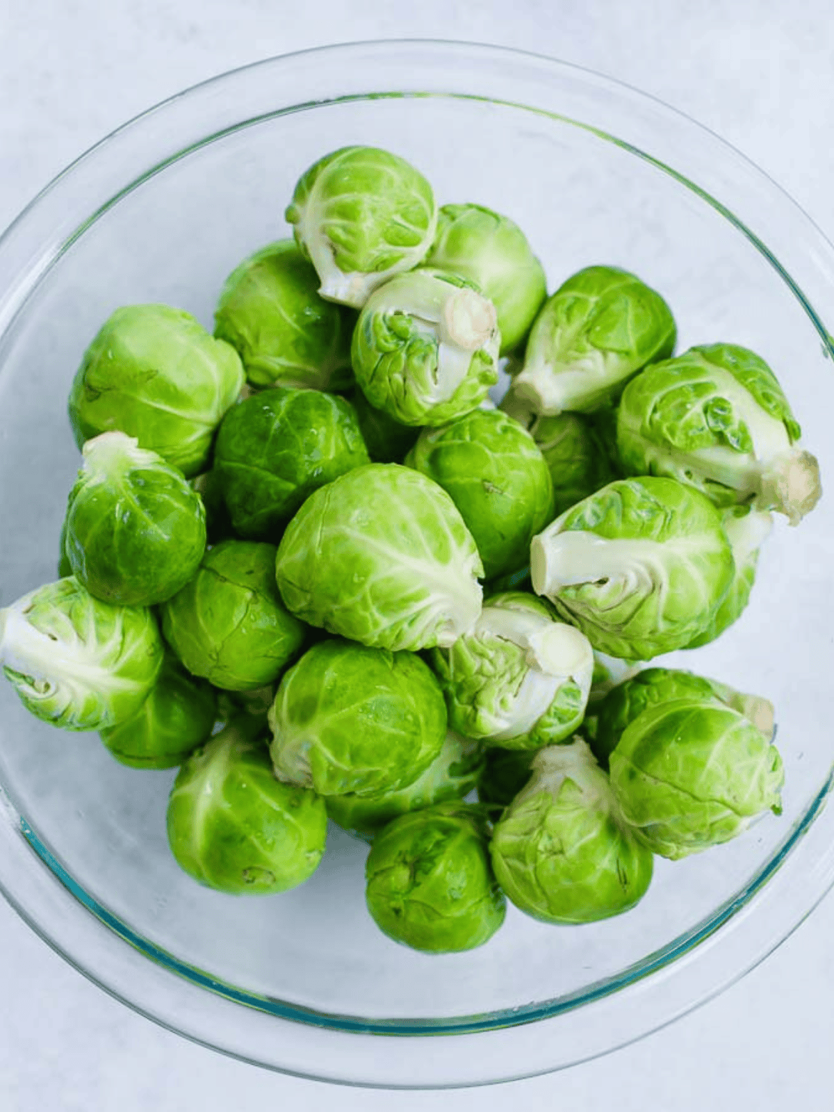 Fresh whole Brussels sprouts in a glass bowl before trimming.
