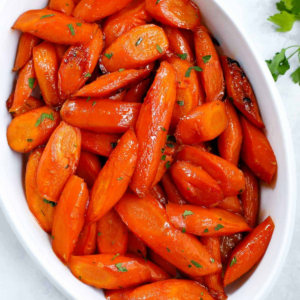 Roasted glazed carrots with browned edges and parsley in a baking dish.