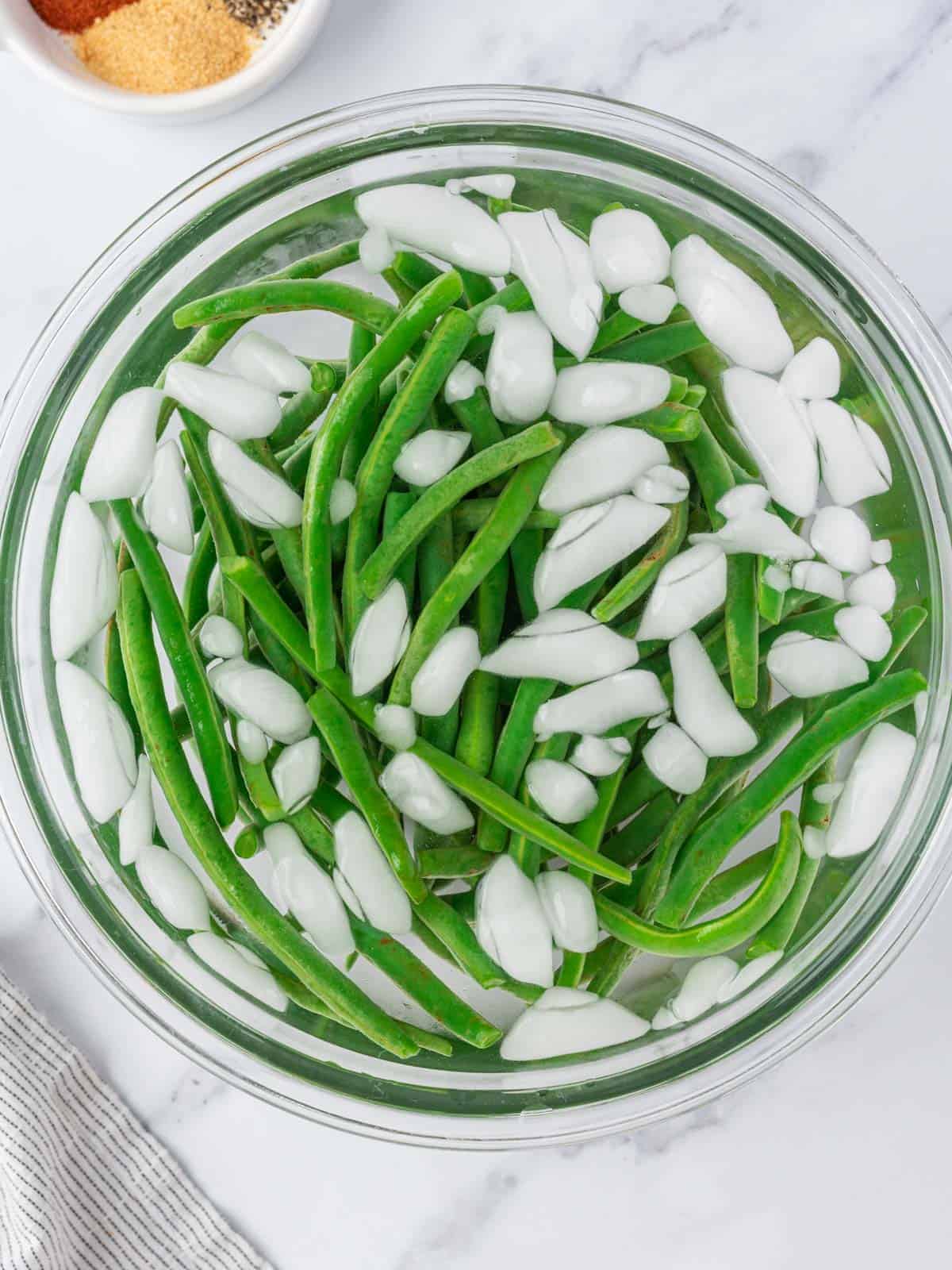 Blanched green beans cooling in a large bowl of ice water.
